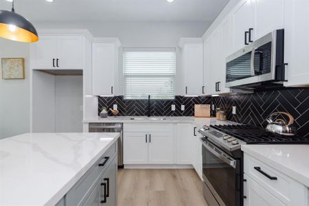 The herringbone-patterned black backsplash adds a touch of timeless elegance, contrasting beautifully with the light-colored countertops.