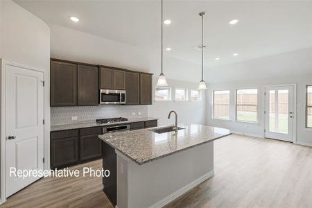 Kitchen with sink, decorative light fixtures, appliances with stainless steel finishes, light hardwood / wood-style flooring, and light stone countertops