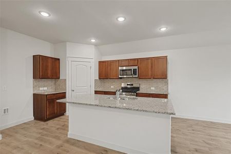 Kitchen featuring backsplash, stainless steel appliances, light wood-type flooring, and a center island with sink