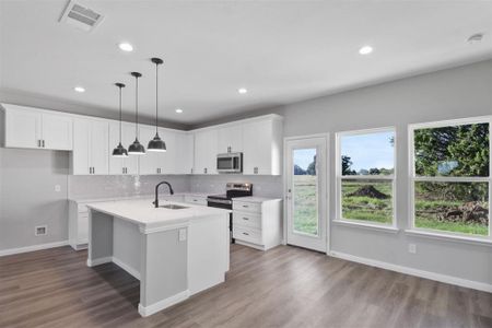 Kitchen featuring stainless steel appliances, sink, hardwood / wood-style flooring, a center island with sink, and white cabinets