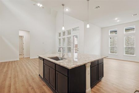 Kitchen with sink, light stone counters, stainless steel dishwasher, decorative light fixtures, and a center island with sink