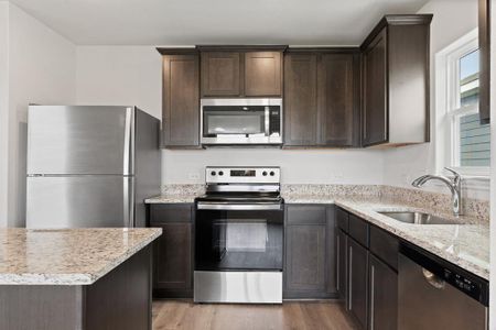 Kitchen featuring light stone countertops, appliances with stainless steel finishes, dark brown cabinetry, sink, and light hardwood / wood-style floors