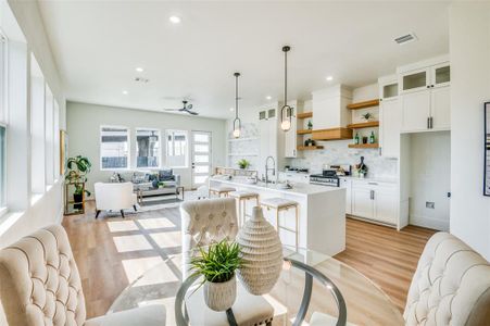 Kitchen featuring light wood-type flooring, a kitchen island with sink, stainless steel stove, hanging light fixtures, and white cabinetry