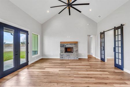 Unfurnished living room with ceiling fan, light wood-type flooring, high vaulted ceiling, and french doors