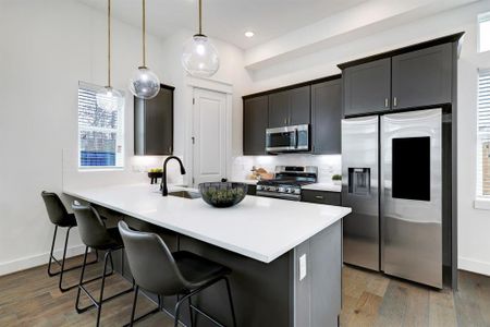 Modern kitchen with sleek dark cabinetry, stainless steel appliances, and elegant pendant lighting over a spacious island with seating.