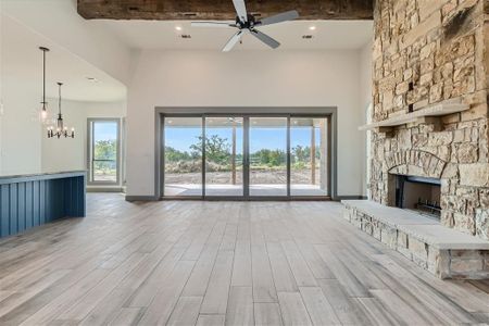 Unfurnished living room featuring light hardwood / wood-style flooring, ceiling fan with notable chandelier, a stone fireplace, beamed ceiling, and a high ceiling