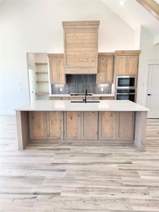 Kitchen with high vaulted ceiling, stainless steel oven, light countertops, built in microwave, and a large island with sink