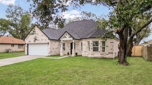 This is a single-story home featuring a stone facade, a two-car garage, and a well-maintained lawn with a mature tree, offering a mix of curb appeal and natural beauty.