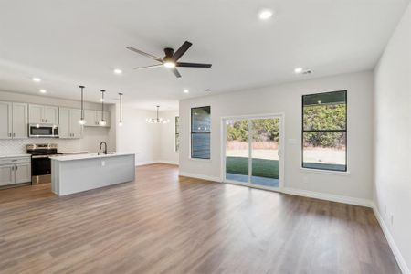 Living room featuring ceiling fan with notable chandelier, light hardwood / wood-style floors, open to the kitchen and dining room