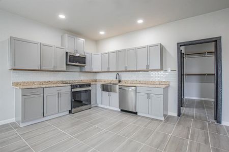 Kitchen with backsplash, light stone countertops, gray cabinets, appliances with stainless steel finishes, and a sink