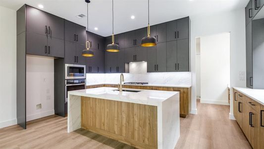 Kitchen featuring an island with sink, stainless steel appliances, decorative light fixtures, and light hardwood / wood-style floors