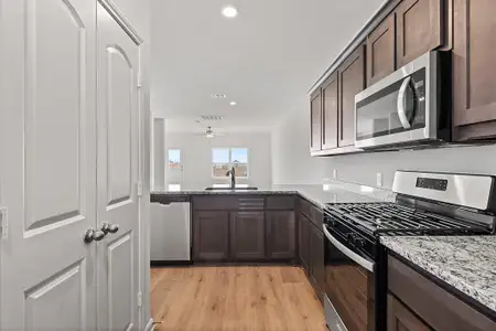 Kitchen with dark brown cabinetry, appliances with stainless steel finishes, light stone counters, and a sink