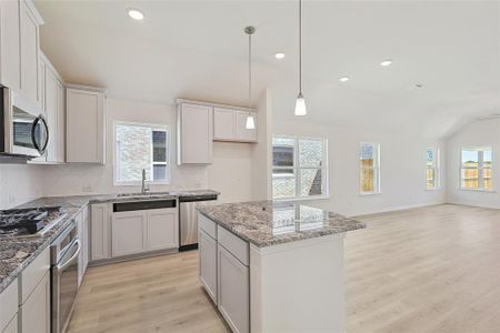 Kitchen with light hardwood / wood-style flooring, vaulted ceiling, a kitchen island, sink, and appliances with stainless steel finishes