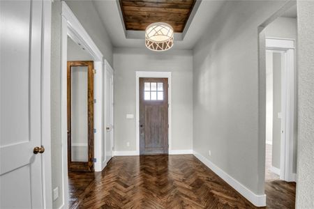 Entrance foyer featuring a raised ceiling, dark parquet floors, and wood ceiling