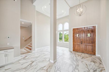 This is a spacious dining area featuring high ceilings, elegant marble flooring, and a chic chandelier. The area is well-lit with natural light from the arched windows, a perfect area to entertain.