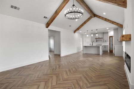 Unfurnished living room featuring an inviting chandelier, dark parquet flooring, and lofted ceiling with beams