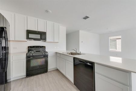 Kitchen with black appliances, kitchen peninsula, sink, light wood-type flooring, and white cabinetry