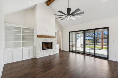 Unfurnished living room with dark hardwood / wood-style flooring, ceiling fan, beam ceiling, high vaulted ceiling, and a stone fireplace