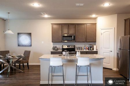 Kitchen with dark hardwood / wood-style floors, an island with sink, stainless steel appliances, and decorative light fixtures