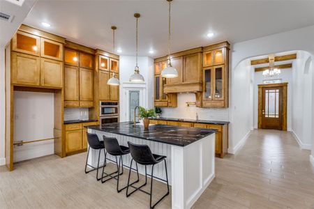 Kitchen featuring light hardwood / wood-style flooring, decorative backsplash, a kitchen island, decorative light fixtures, and stainless steel double oven