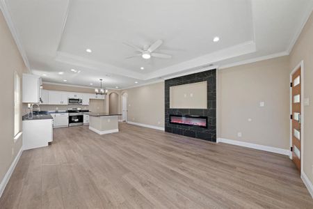 Unfurnished living room featuring baseboards, a premium fireplace, a raised ceiling, and light wood-style floors