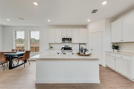 Kitchen with appliances with stainless steel finishes, white cabinets, a center island with sink, and light wood-type flooring