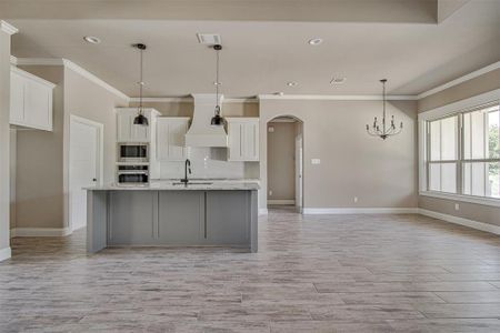 Kitchen featuring a kitchen island with sink, stainless steel appliances, premium range hood, light stone counters, and decorative light fixtures