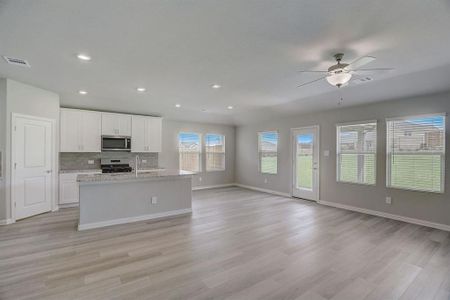 Kitchen featuring light wood-type flooring, light stone counters, tasteful backsplash, white cabinets, and appliances with stainless steel finishes