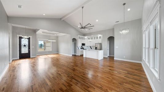 Unfurnished living room featuring visible vents, arched walkways, wood finished floors, and ceiling fan with notable chandelier