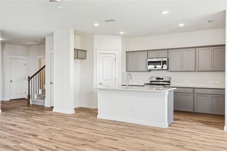 Kitchen featuring backsplash, light hardwood / wood-style flooring, an island with sink, stainless steel appliances, and gray cabinets