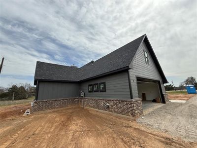 View of home's exterior with brick siding, a shingled roof, a garage, and dirt driveway