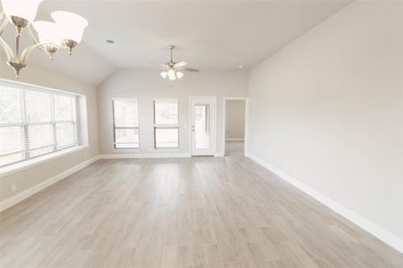 Unfurnished living room with ceiling fan with notable chandelier, vaulted ceiling, and light hardwood / wood-style flooring