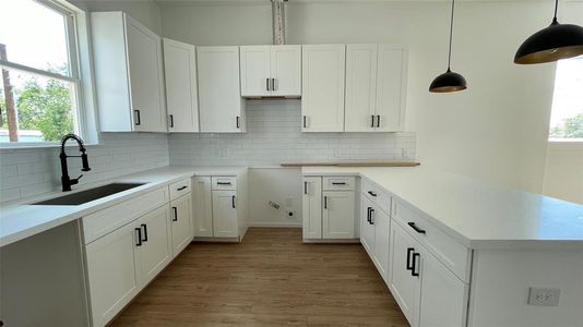 kitchen featuring white shaker cabinets, sleek black hardware, subway tile backsplash, and quartz countertops. It's equipped with a deep sink and has ample storage space.