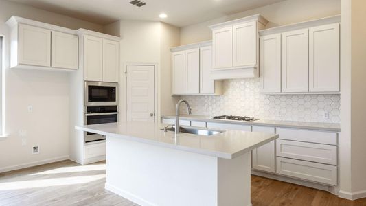 Kitchen featuring sink, white cabinetry, an island with sink, built in microwave, and stainless steel oven