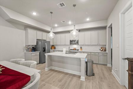 Kitchen featuring a center island with sink, appliances with stainless steel finishes, sink, decorative light fixtures, and light hardwood / wood-style floors