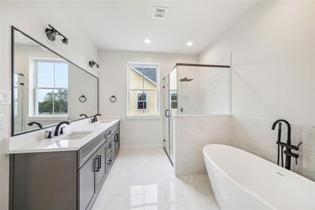 This modern bathroom features a spacious layout with a double vanity, large mirrors, a sleek glass-enclosed shower, and a freestanding bathtub. Natural light fills the room through two windows, highlighting the elegant fixtures and finishes.