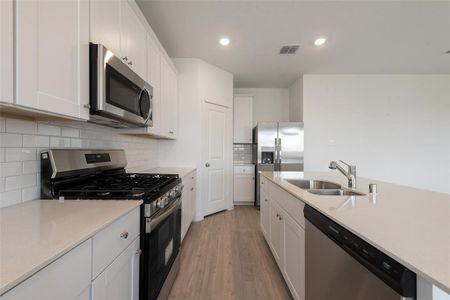 Kitchen with stainless steel appliances, white cabinets, light wood-type flooring, and sink