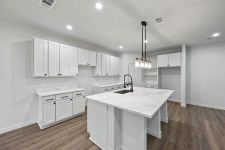 Kitchen featuring hanging light fixtures, sink, an island with sink, and white cabinets