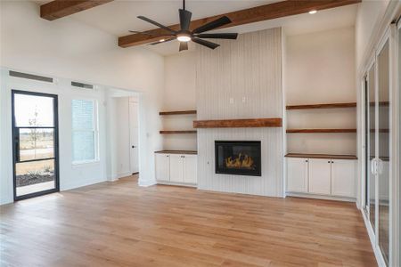 Unfurnished living room with a towering ceiling, a fireplace, ceiling fan, beam ceiling, and light wood-type flooring