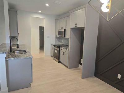 Kitchen featuring sink, decorative backsplash, custom granite countertops, light laminate floors, and stainless steel range oven