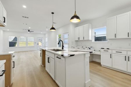 Kitchen with sink, decorative light fixtures, an island with sink, and white cabinets