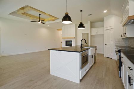 Kitchen featuring light wood-type flooring, sink, a raised ceiling, a center island with sink, and appliances with stainless steel finishes