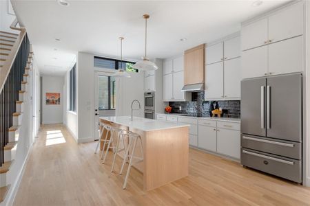 Kitchen with decorative light fixtures, light hardwood / wood-style floors, stainless steel appliances, a breakfast bar area, and an island with sink