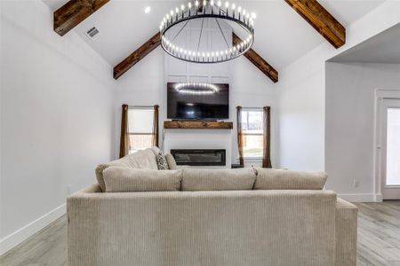 Unfurnished living room featuring baseboards, visible vents, a glass covered fireplace, beamed ceiling, and a notable chandelier