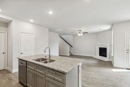 Kitchen featuring light stone countertops, sink, stainless steel dishwasher, an island with sink, and light wood-type flooring