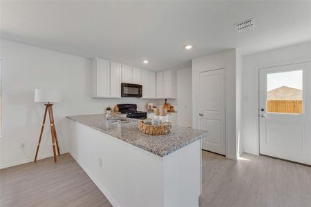 Kitchen with light hardwood / wood-style floors, white cabinets, kitchen peninsula, light stone countertops, and black appliances