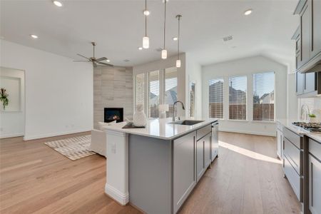 Kitchen with gray cabinetry, ceiling fan, hanging light fixtures, a fireplace, and a center island with sink