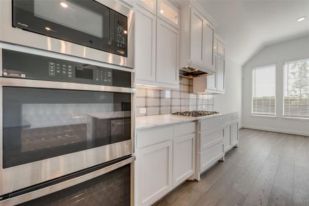 Kitchen with stainless steel appliances, light stone countertops, white cabinets, light wood-type flooring, and backsplash