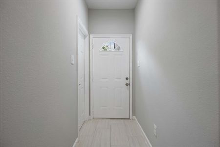 A welcoming entryway features a white front door with a decorative window, neutral gray walls, and light tile flooring, creating a bright and inviting atmosphere.