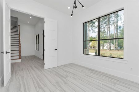 Large windows with a view of trees, a staircase to the second level, and sleek, light tile wood-look flooring. It's a blank canvas ready for personalization.